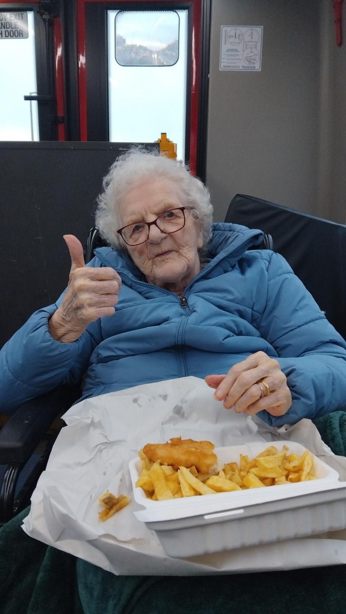 Photo of a woman smiling and doing a thumbs up whilst having fish and chips