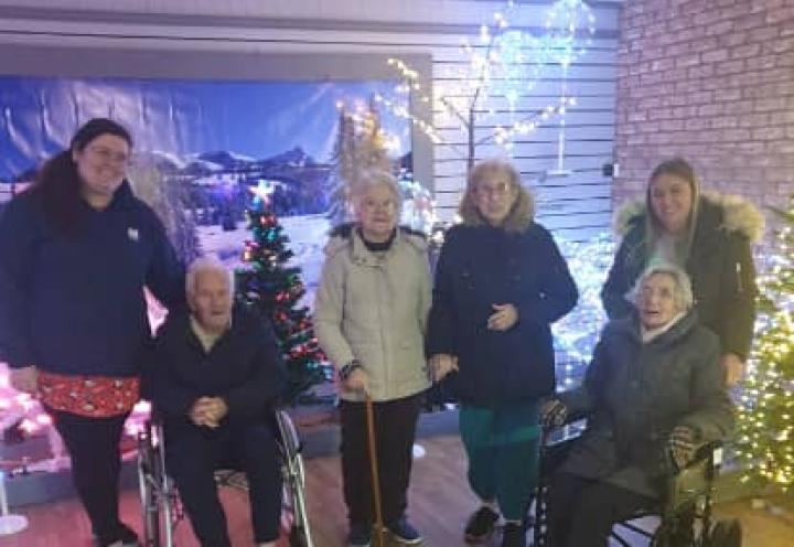 residents and staff stood in front of the christmas lights at the garden centre. 
