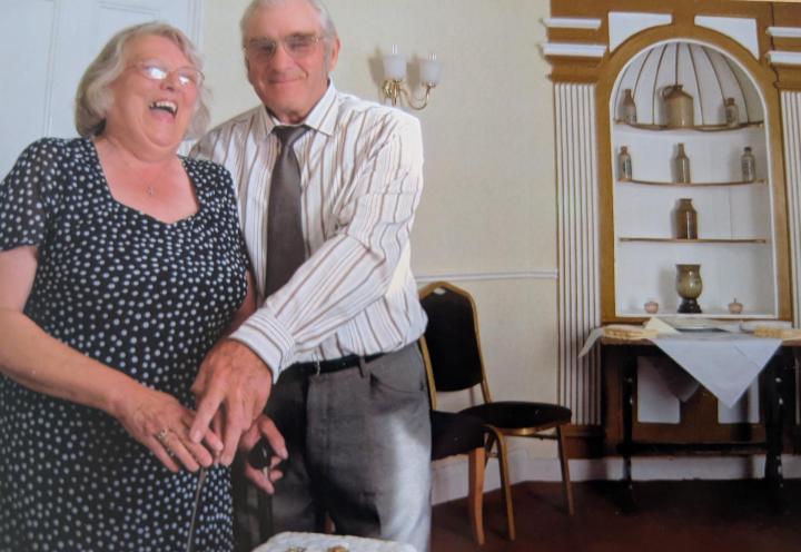 Photo of couple laughing whilst cutting cake