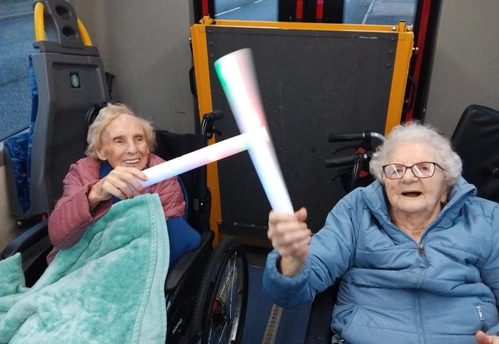 photo of 2 people smiling, holding glow sticks on a bus