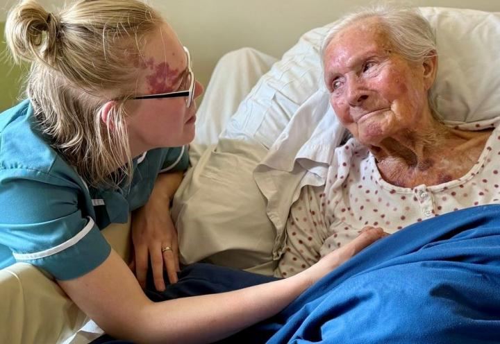 Photo of 2 people smiling, one of them is in bed (rene) and a care colleague is by her smiling
