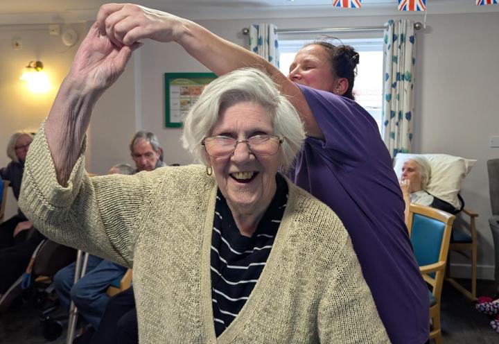 Photo of lady resident smiling and dancing with activity coordinator